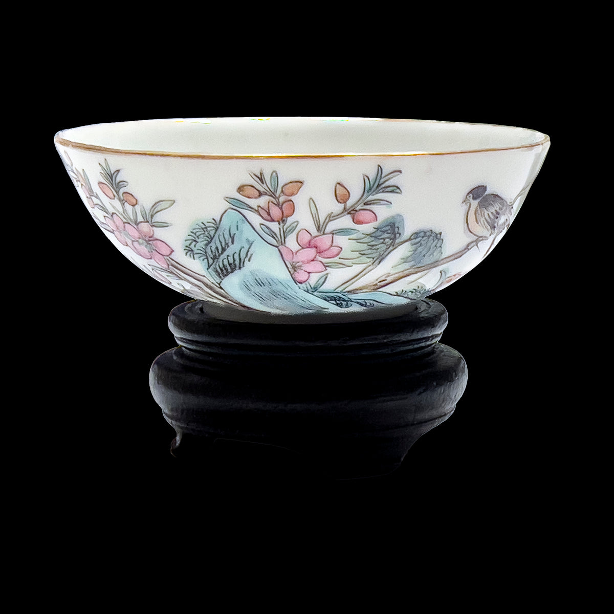 An antique Chinese famille rose porcelain 3.5 inch teacup featuring a hand-painted songbird and pink floral blossoms with a gilded gold rim on a custom carved dark wooden base.