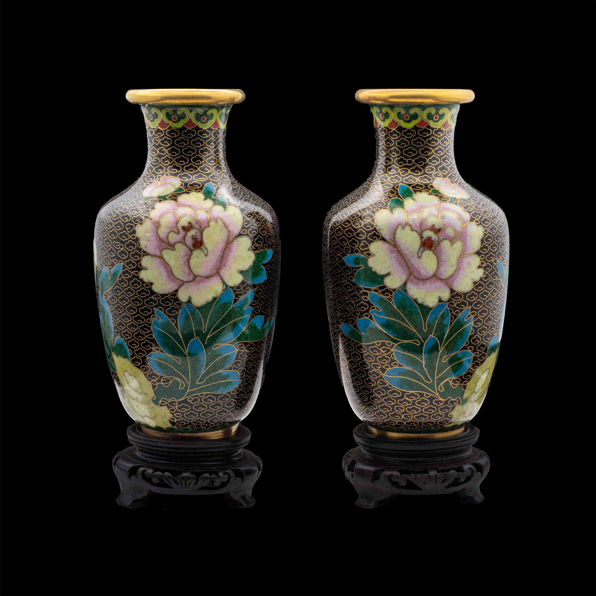 A pair of vintage cloisonné baluster vases featuring hand-enamelled pink peonies over a black cloud pattern ground with gilded rims on carved dark wood display pedestals.
