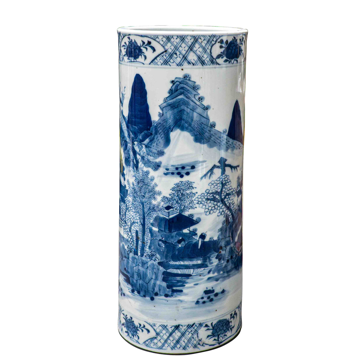 A full front view of a cylindrical 19th-century Chinese blue and white porcelain hat stand against a black background. The underglaze cobalt blue painting highlights sweeping, triangular mountain peaks rising behind a cluster of leafy pine trees and a small traditional house. Intricate cross-hatch patterned geometric borders wrap around the top and lower base.
