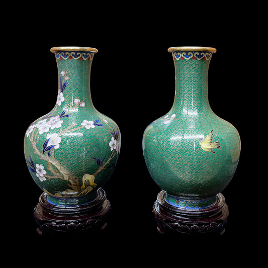 A pair of vintage Chinese cloisonne green enamel baluster vases on wood stands, showing a rotated multi-angle view of hand-detailed floral branches and a gilded flying swallow motif.
