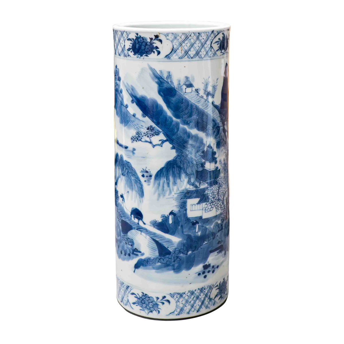 A 19th-century Chinese blue and white porcelain cylindrical hat stand photographed against a white background. The hand-painted cobalt blue decoration depicts a traditional Shan Shui mountain landscape. A figure walks across a stone bridge spanning a river, leading toward a multi-story pavilion nestled in stylized hills and pine trees. Decorative cross-hatch and floral ruyi diaper bands border the top and bottom rims.