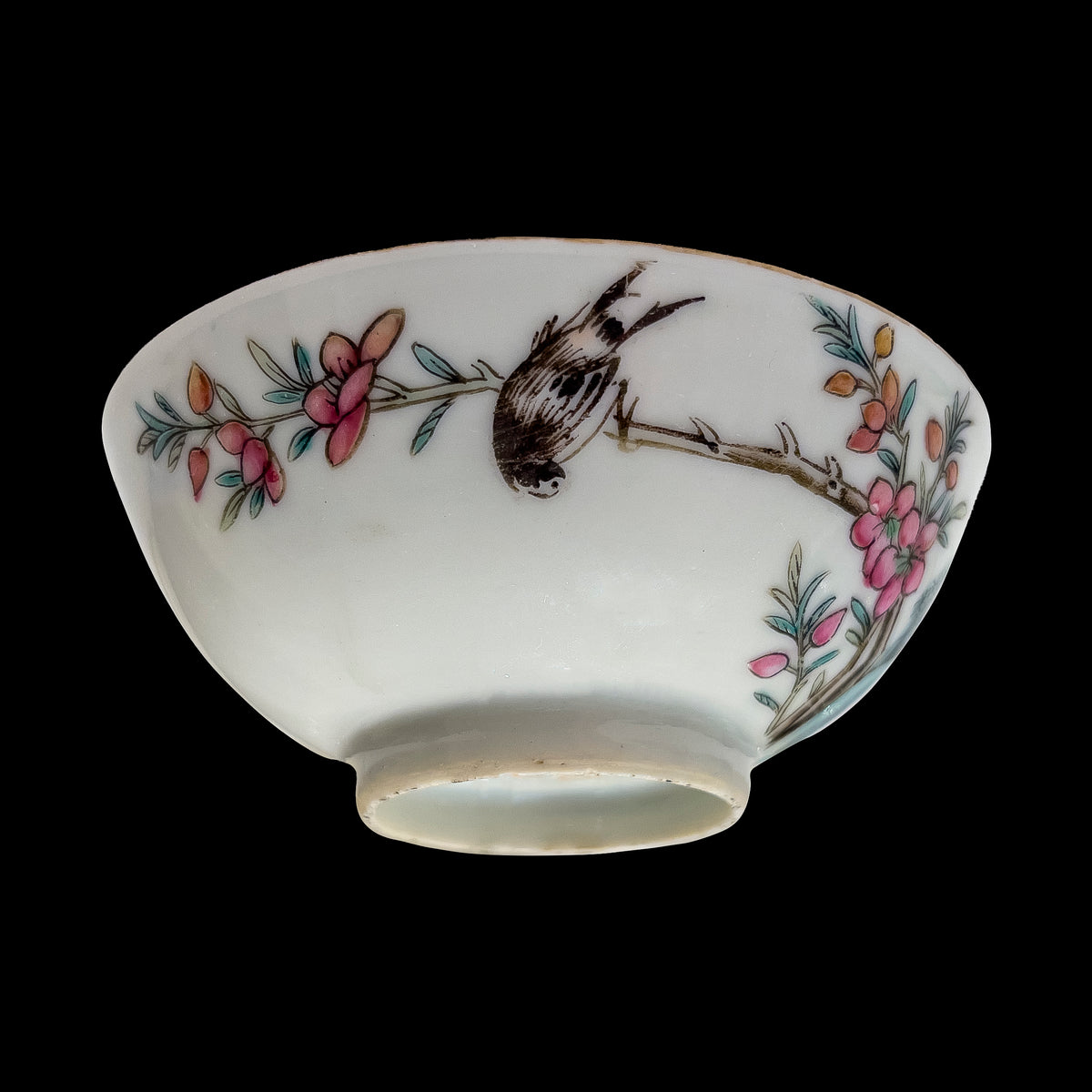 A reverse side studio profile of an antique Chinese famille rose porcelain 3.5 inch wine cup featuring a hand-painted swallow bird perched upside down on a blooming plum branch.