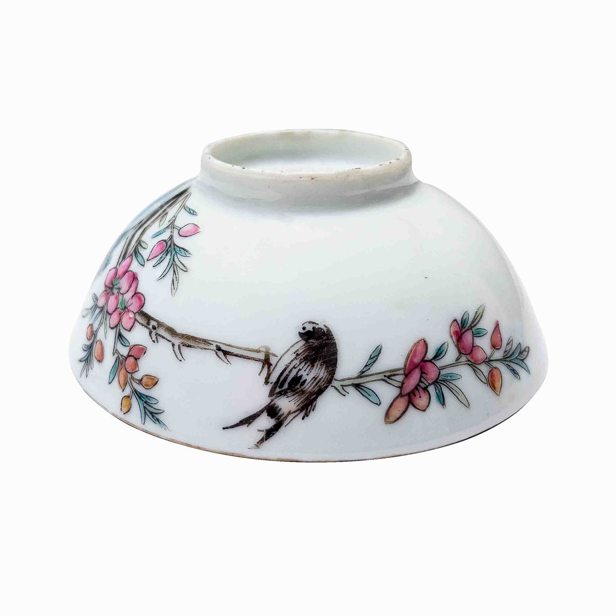 A close up macro shot of an antique Chinese porcelain wine cup inverted showcasing a bird on a pink multi blossom branch.