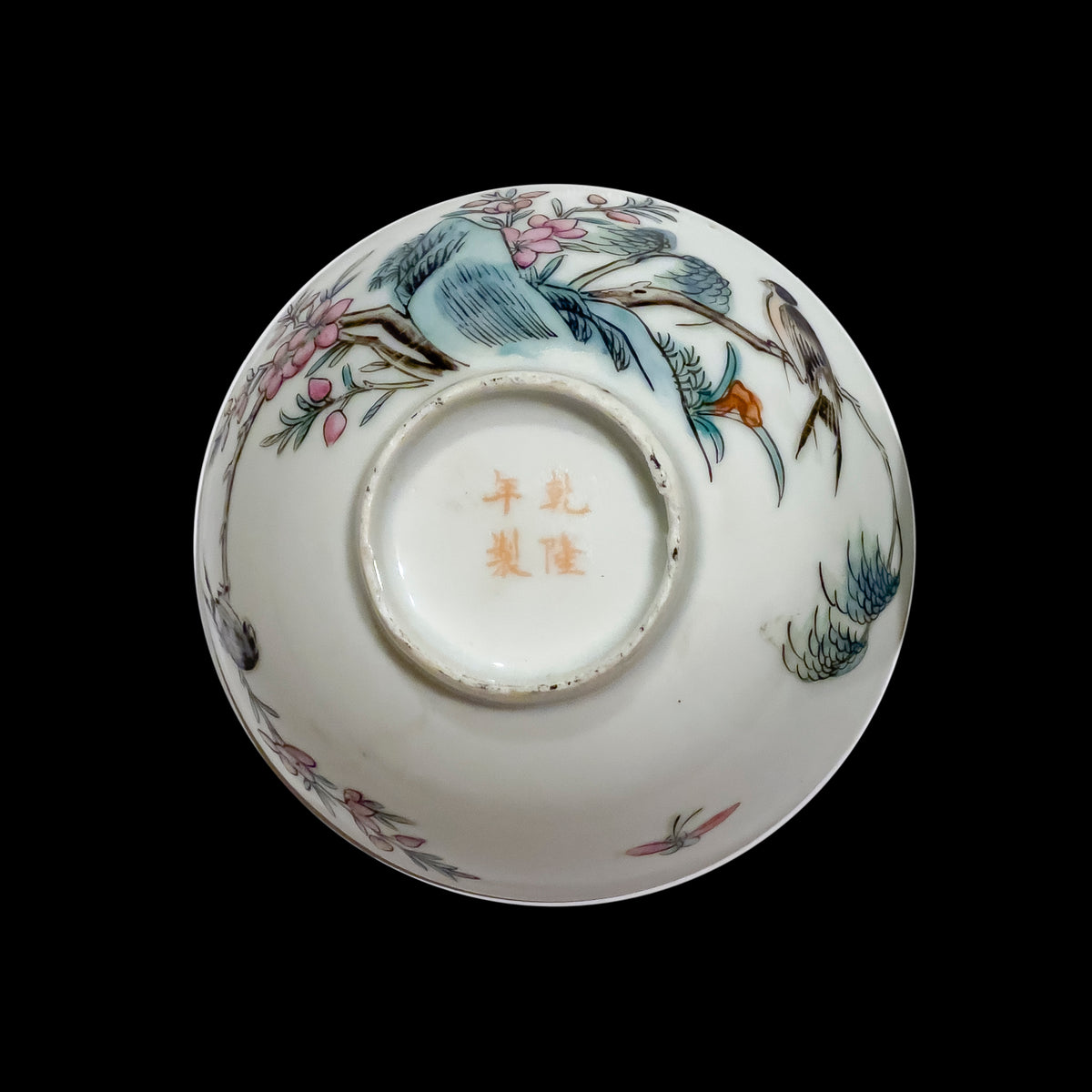 A close up macro shot of an antique Chinese porcelain teacup base showcasing a red hand-painted four-character Qianlong Nian Zhi mark within a circular unglazed foot rim.
