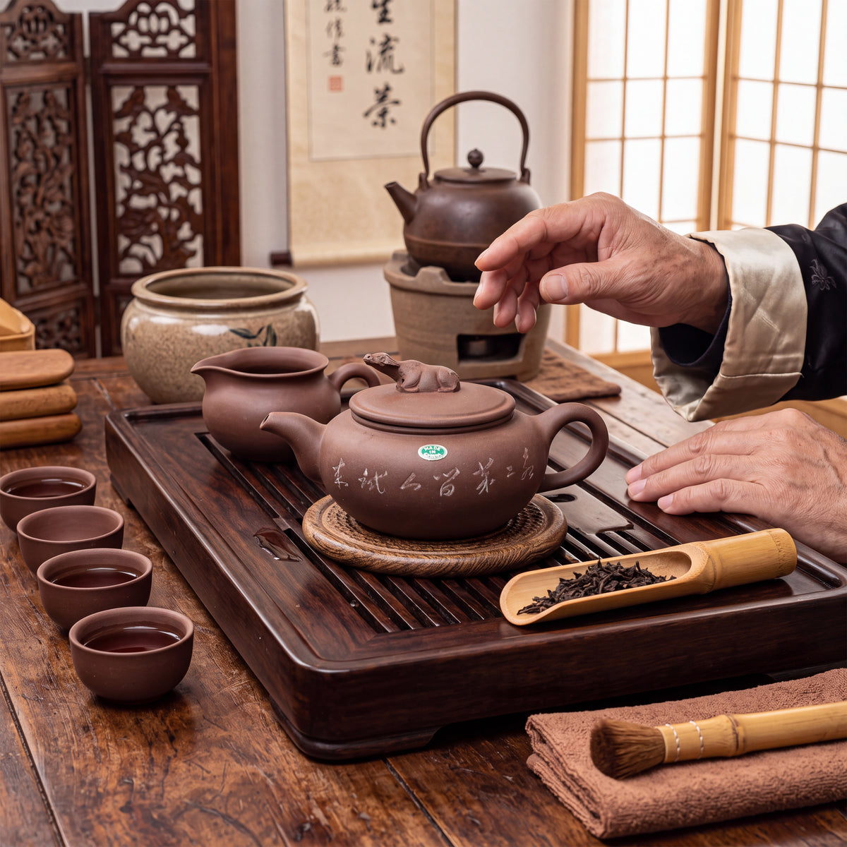 A zisha clay teapot with a sculpted animal water buffalo figure on the lid, featuring engraved Chinese characters on the side. The set includes three small matching tea cups filled with amber liquid, a wooden tea tray, a scoop, a brush, and tongs.
