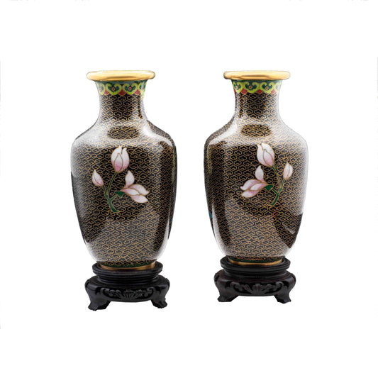 A pair of vintage cloisonné baluster vases showing the reverse side hand-enamelled white magnolia flower blossoms over a black cloud ground on carved wooden pedestals.