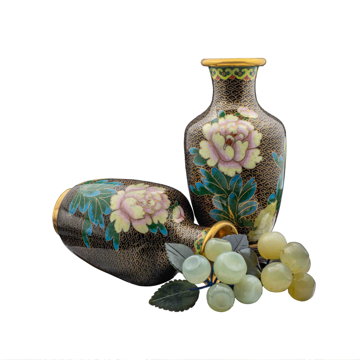 A pair of vintage cloisonné black enamel peony baluster vases styled with one vase upright and one horizontal, decorated with a cluster of carved jade grapes against a white background.