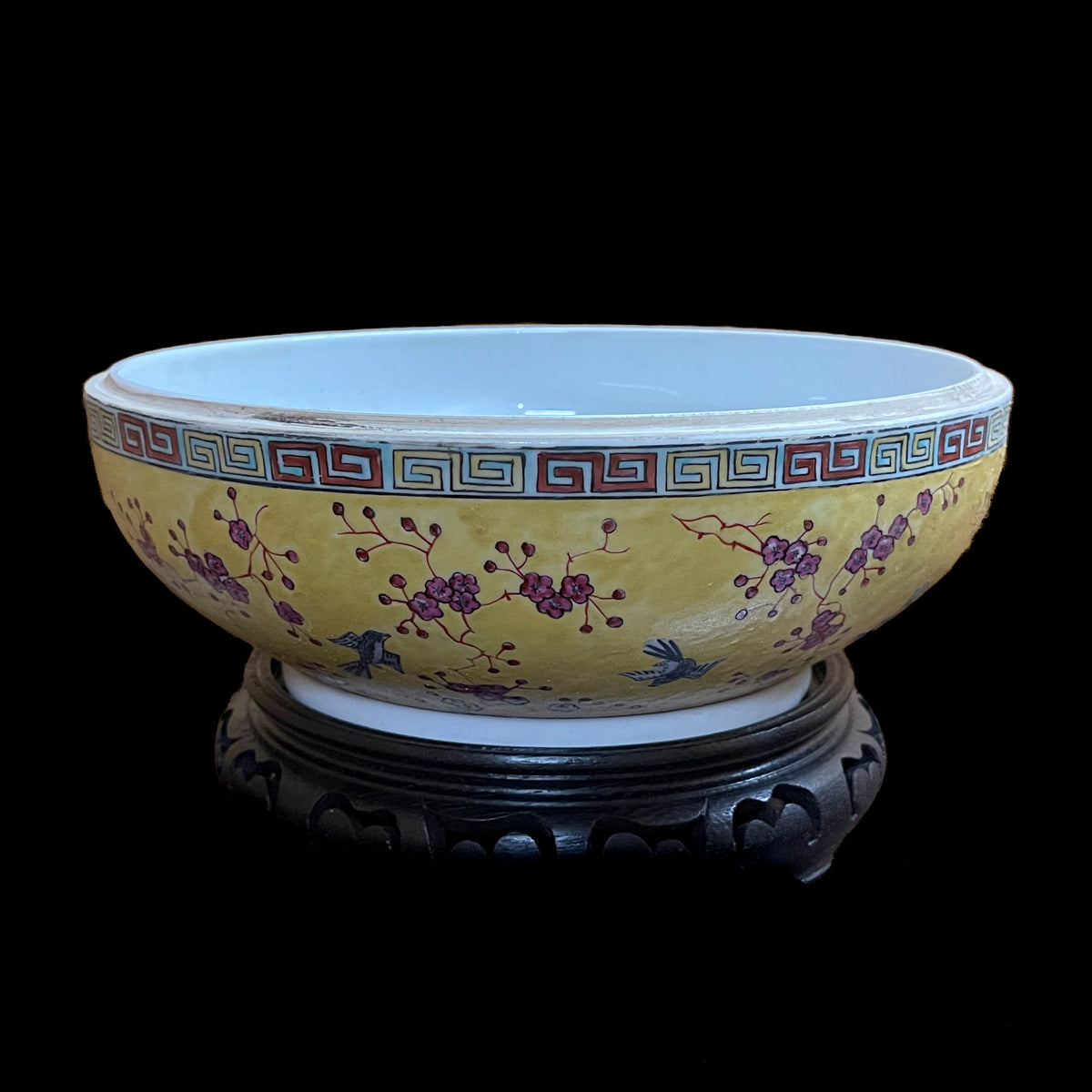 An open bowl view of a vintage Chinese porcelain sweetmeat container base showing a white glazed interior, plum blossoms on an imperial yellow ground, and a carved wood stand.